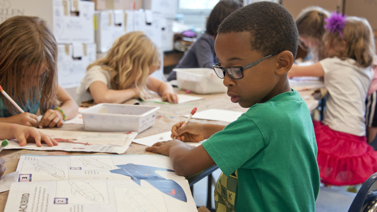 Black boy writing at school desk.