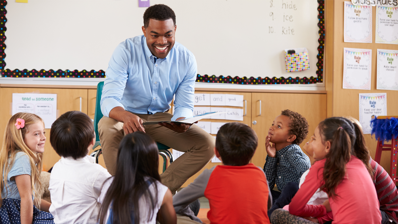 Black male teacher reading to young students