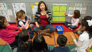 kindergarten teacher provides instruction to small group of students on classroom floor