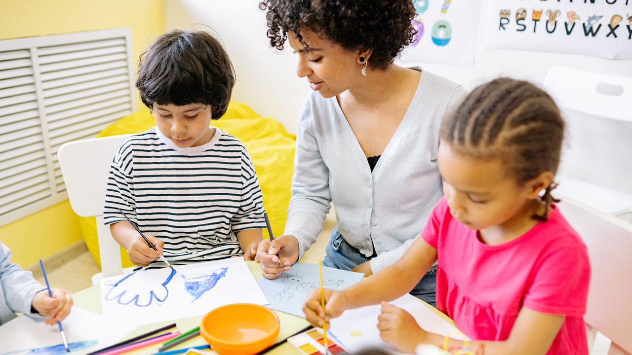 teacher doing a painting activity with two preschool students